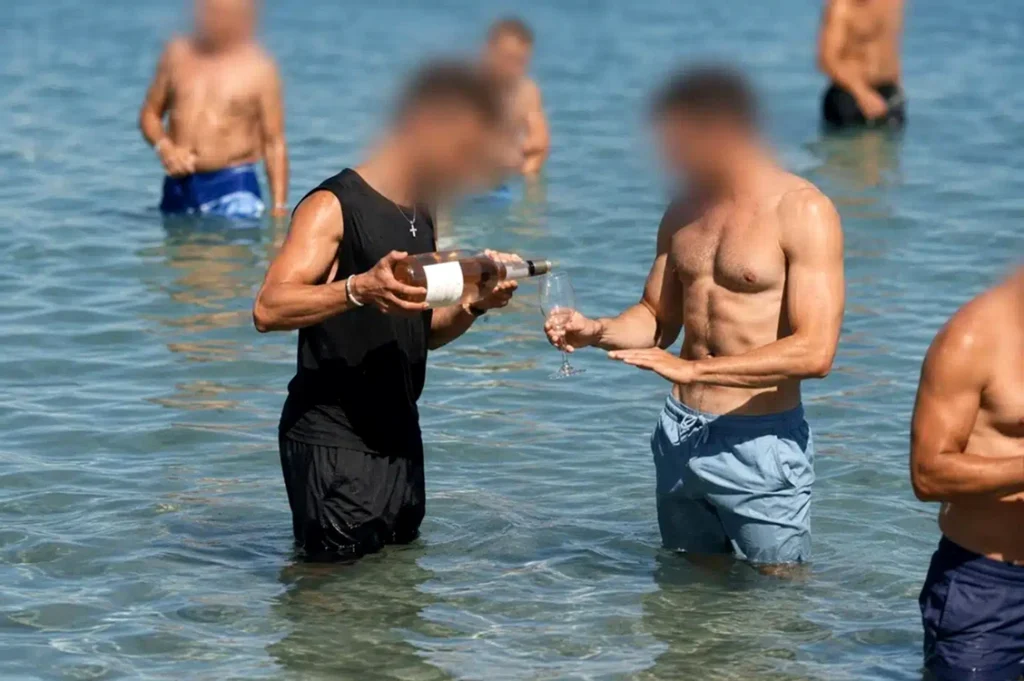 Scenă controversată pe o plajă din Grecia. Ospătarul merge prin apă cu vinul pentru turiști